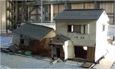 Photo of a wooden house reinforced against earthquakes and an unreinforced wooden house side by side in a shaking table experiment.